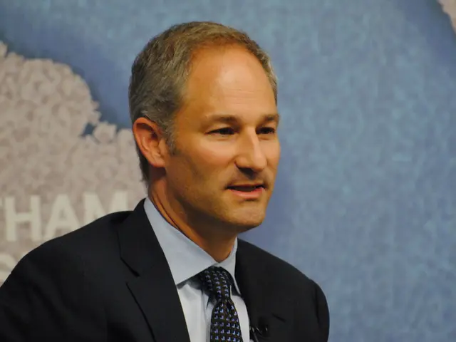 In this image there is a man who is wearing the black suit and a tie. In the background there is a...