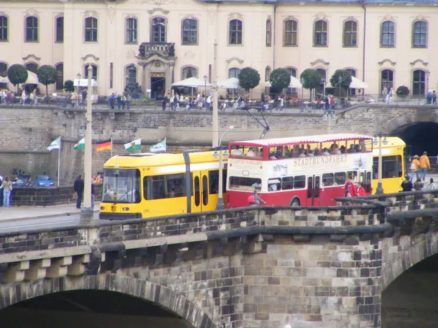 In this image we can see group of vehicles parked on the bridge, a group of people is standing. In...