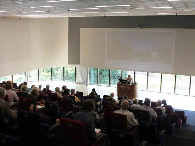It is a seminar hall in a University , lot of people are sitting in the chairs and paying attention...